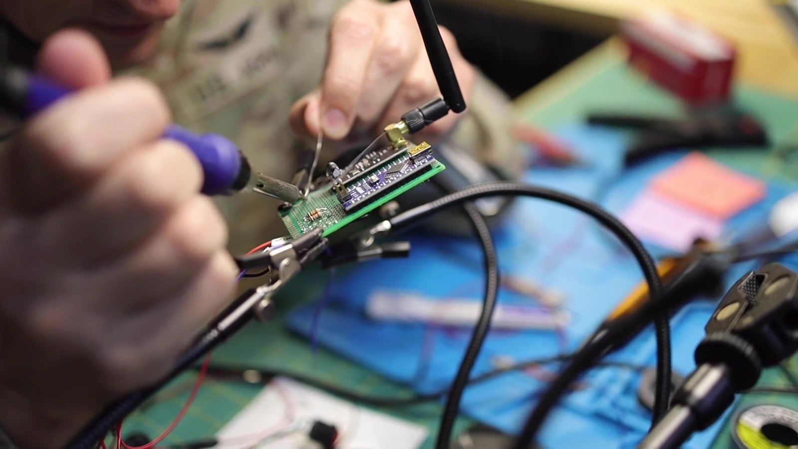 Close-up of a uniformed engineer testing a circuit board at an electronics workbench.