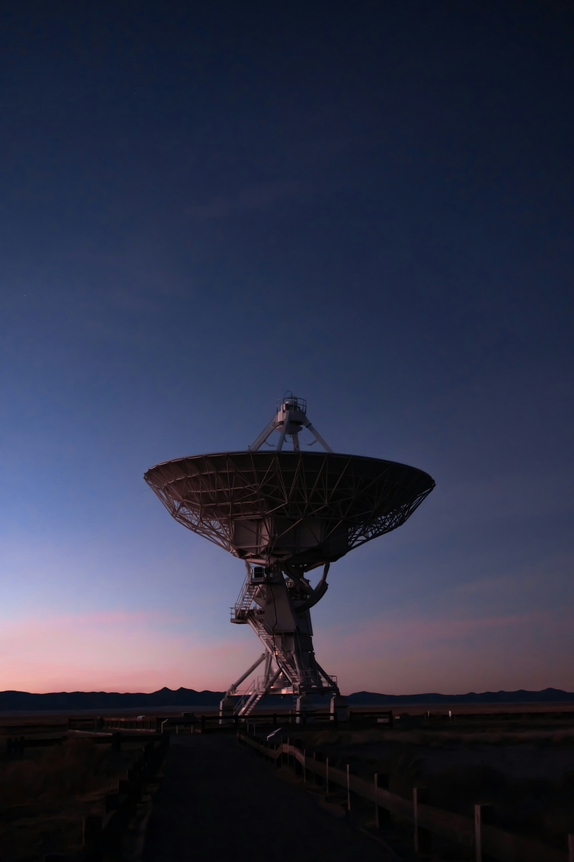 A large radio telescope beneath a blue and pink twilight sky.