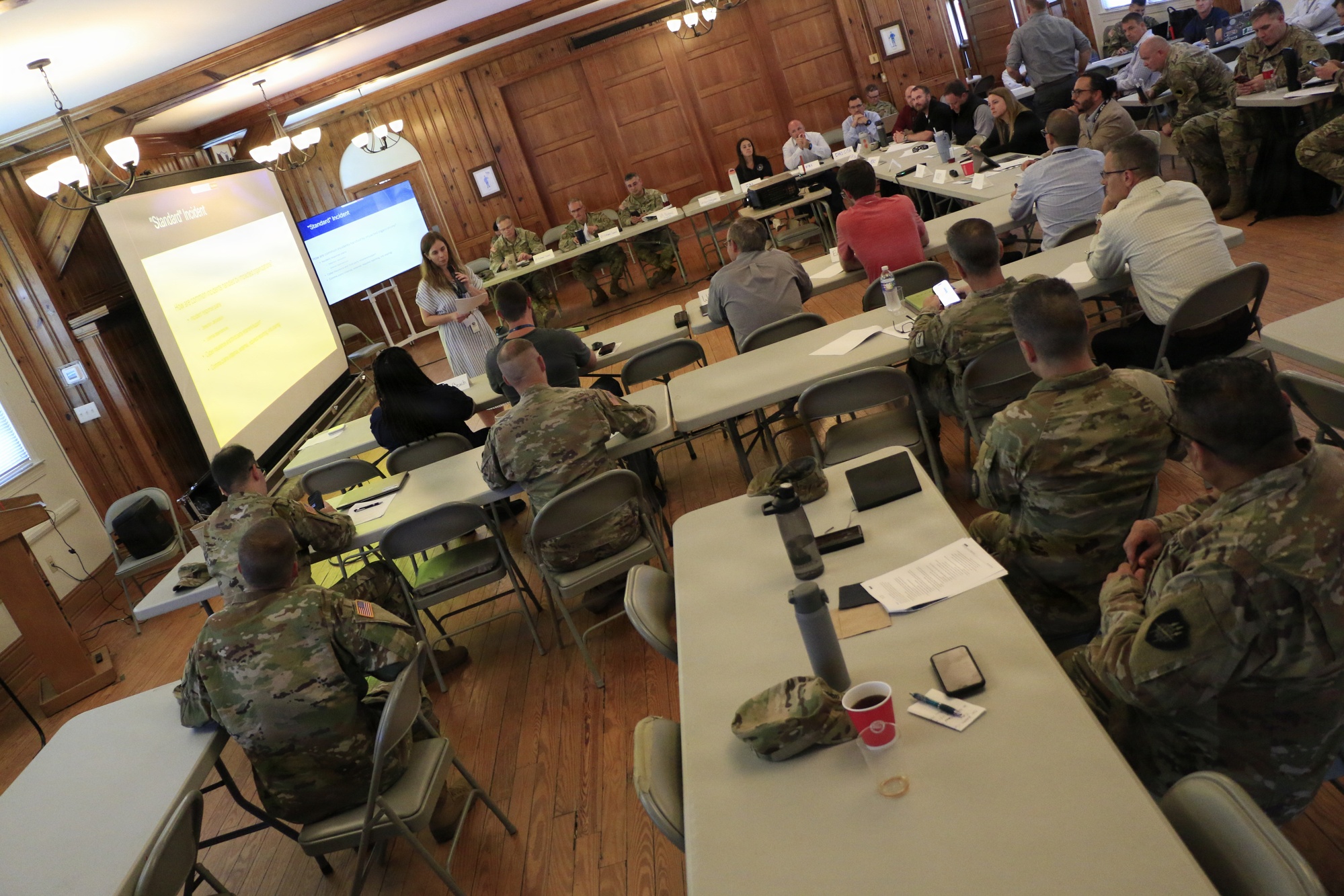 Civilian and uniformed cyber specialists take part in a collaborative tabletop exercise in a wood-paneled planning room.